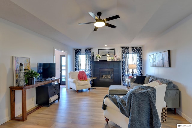 living room featuring ceiling fan, a tile fireplace, and light hardwood / wood-style flooring