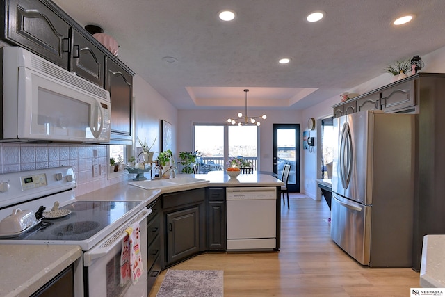 kitchen with pendant lighting, white appliances, sink, light wood-type flooring, and a notable chandelier