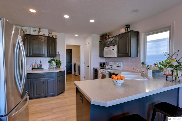 kitchen featuring sink, kitchen peninsula, light hardwood / wood-style floors, white appliances, and decorative backsplash