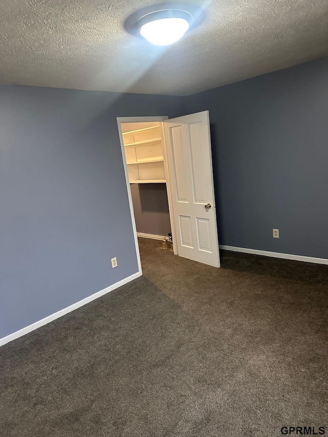 unfurnished bedroom featuring dark colored carpet, a walk in closet, a textured ceiling, and a closet