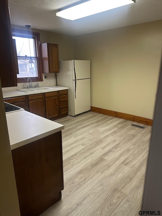 kitchen with pendant lighting, sink, light wood-type flooring, a textured ceiling, and white fridge