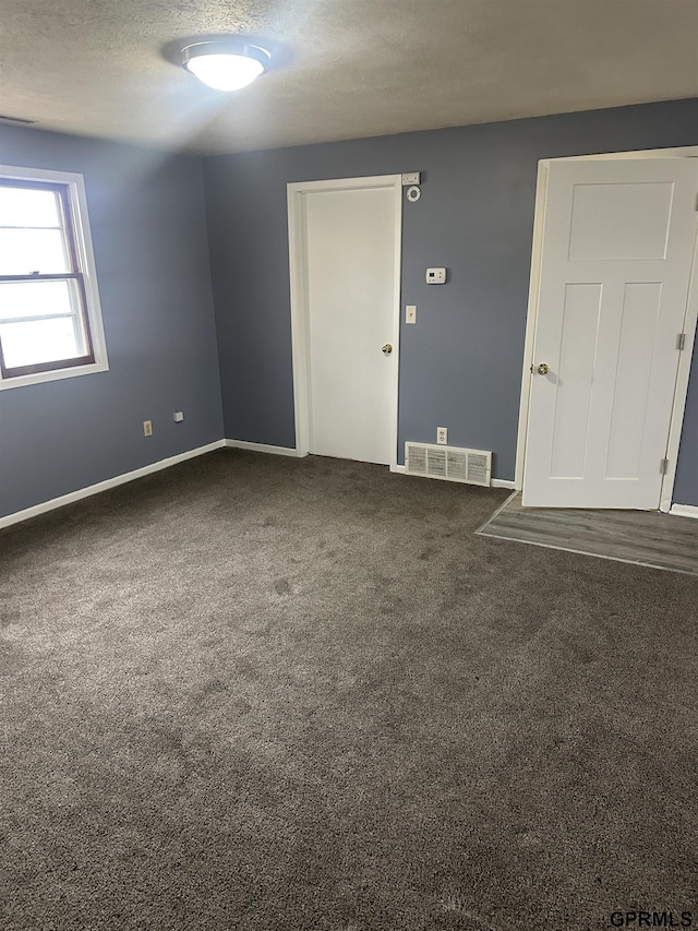 spare room with dark carpet and a textured ceiling