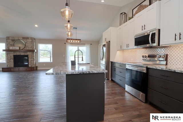 kitchen featuring decorative light fixtures, white cabinets, stainless steel appliances, and vaulted ceiling