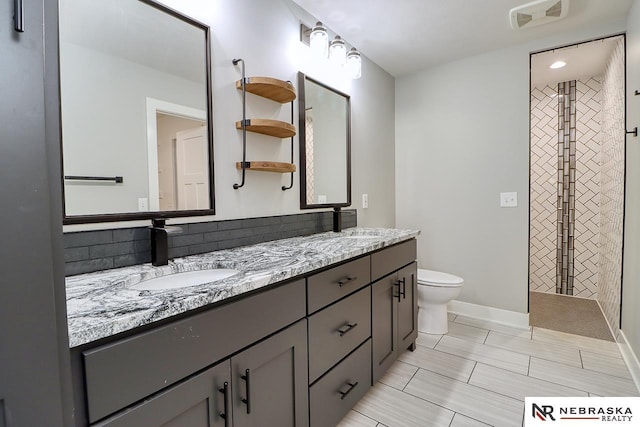 bathroom with a tile shower, vanity, and toilet