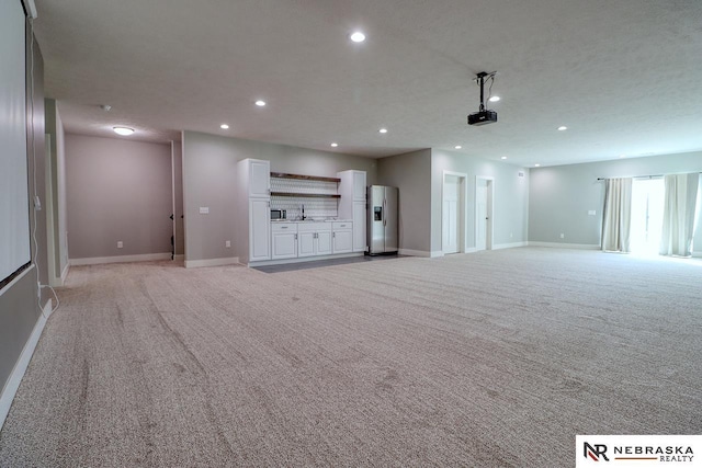 unfurnished living room featuring a textured ceiling, light colored carpet, and sink