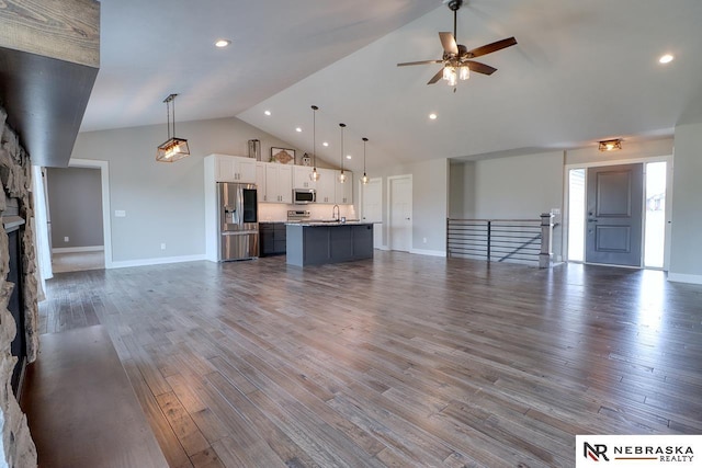 unfurnished living room featuring ceiling fan, sink, hardwood / wood-style flooring, a stone fireplace, and lofted ceiling