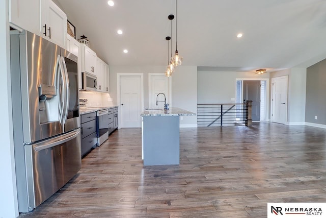 kitchen with stainless steel appliances, a kitchen island with sink, light hardwood / wood-style floors, white cabinetry, and hanging light fixtures