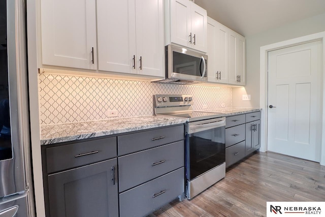 kitchen with light stone countertops, appliances with stainless steel finishes, light wood-type flooring, backsplash, and white cabinetry