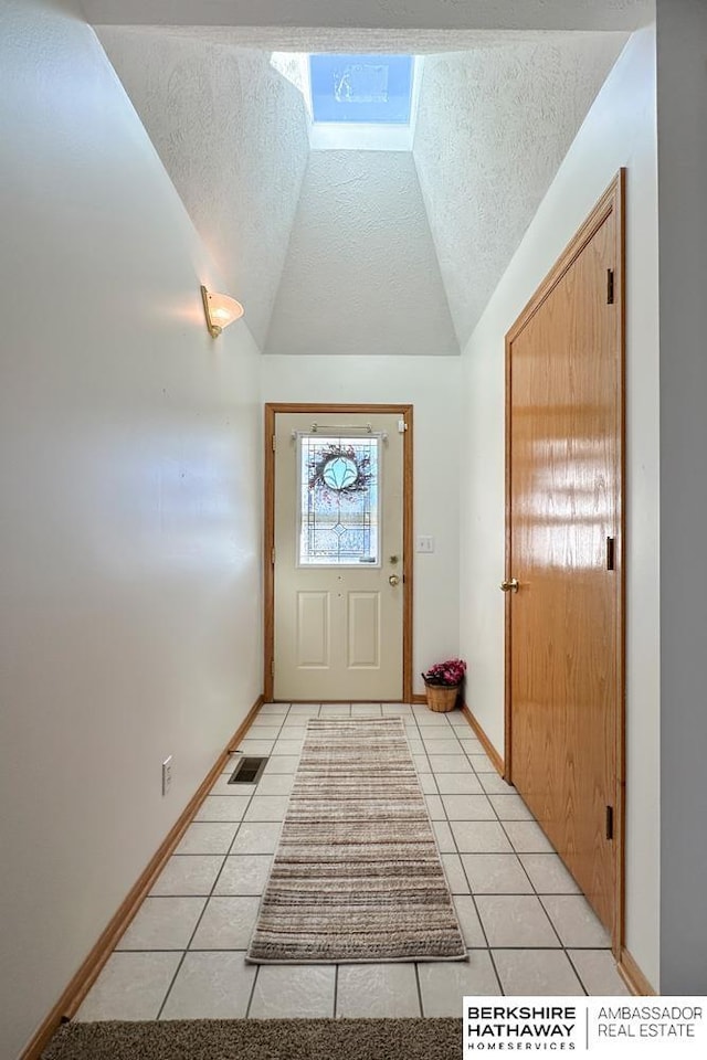 doorway to outside with lofted ceiling, light tile patterned floors, and a textured ceiling