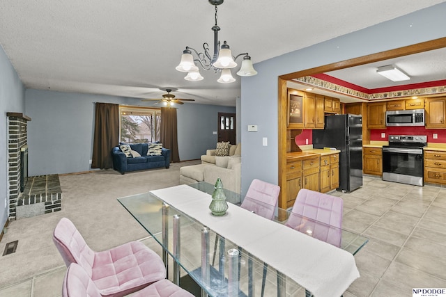 dining area featuring ceiling fan with notable chandelier, light tile patterned flooring, a textured ceiling, and a fireplace