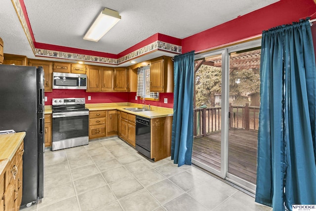 kitchen with sink, light tile patterned flooring, black appliances, and a textured ceiling