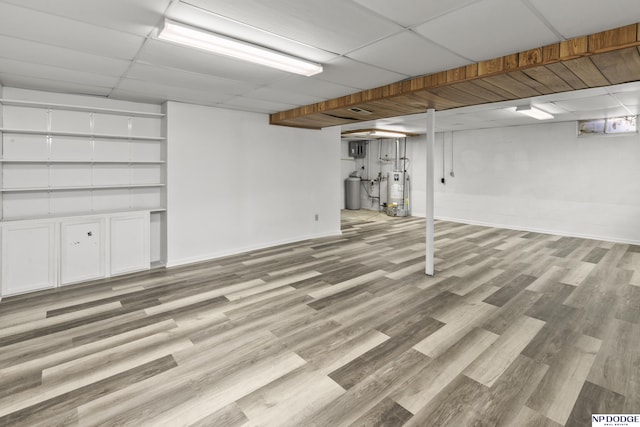 basement featuring a paneled ceiling, light hardwood / wood-style floors, and water heater