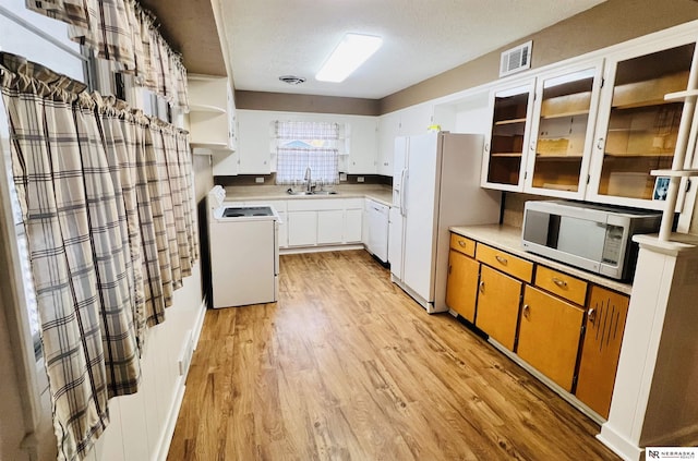 kitchen with light wood-type flooring, a textured ceiling, white appliances, sink, and white cabinetry