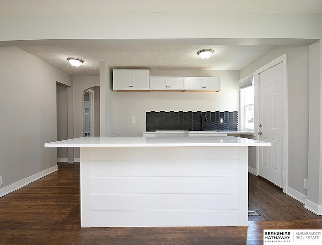 kitchen featuring a textured ceiling, dark wood-type flooring, a spacious island, sink, and white cabinetry