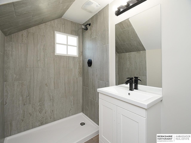 bathroom featuring vanity, a tile shower, and vaulted ceiling