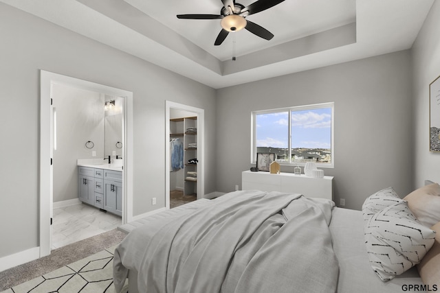 bedroom featuring ceiling fan, a raised ceiling, ensuite bathroom, a walk in closet, and a closet