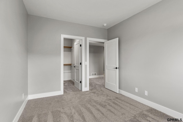 unfurnished bedroom featuring a walk in closet, a closet, and light colored carpet