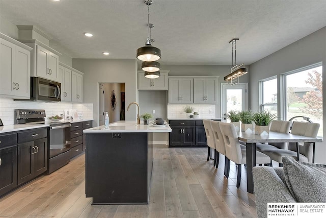 kitchen featuring hanging light fixtures, light hardwood / wood-style floors, stainless steel electric stove, and an island with sink