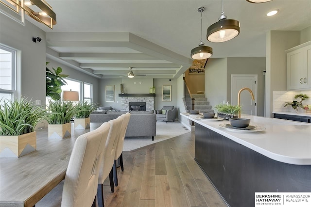 dining area featuring ceiling fan, a fireplace, beamed ceiling, and light wood-type flooring