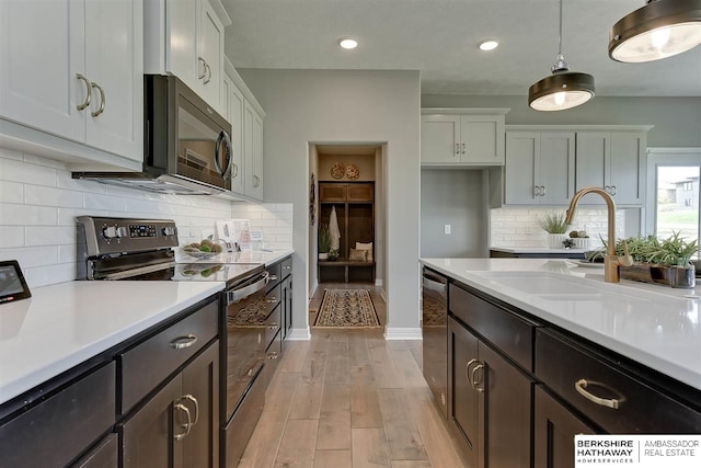 kitchen with white cabinets, pendant lighting, light wood-type flooring, and appliances with stainless steel finishes