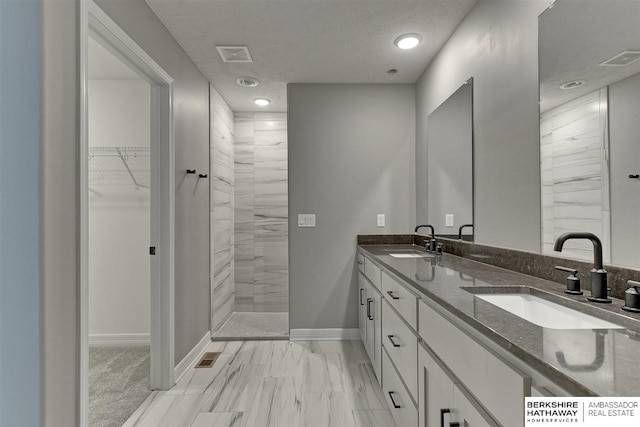 bathroom with a tile shower, vanity, and a textured ceiling