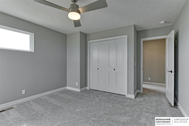 unfurnished bedroom featuring a textured ceiling, ceiling fan, light carpet, and a closet