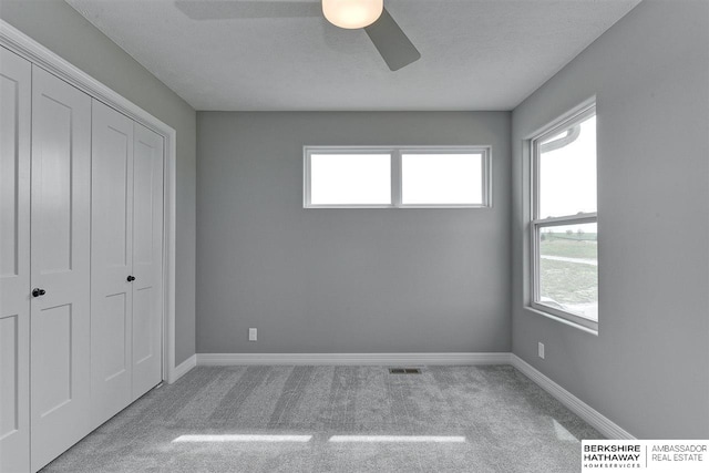 unfurnished bedroom with a closet, a textured ceiling, light colored carpet, and ceiling fan