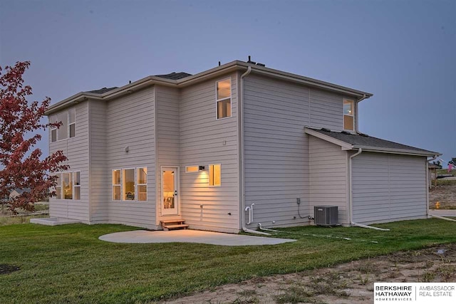 back house at dusk with a patio area, a yard, and central air condition unit