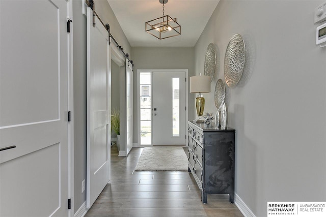 entryway with a barn door, wood-type flooring, and a notable chandelier