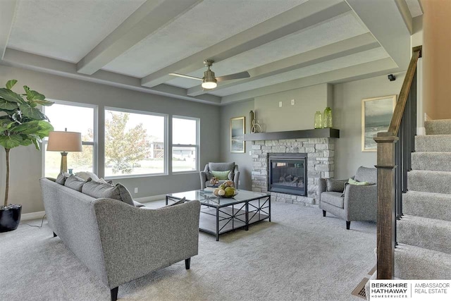 living room featuring beamed ceiling, ceiling fan, a fireplace, and light carpet