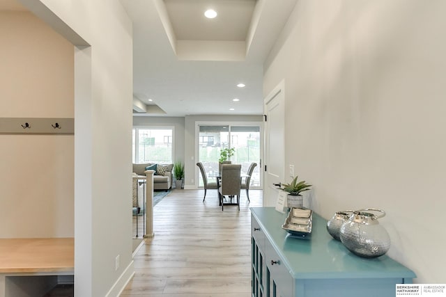 hallway with light wood-type flooring and a tray ceiling