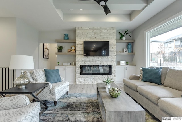 living room featuring a tray ceiling, a fireplace, ceiling fan, and light hardwood / wood-style flooring