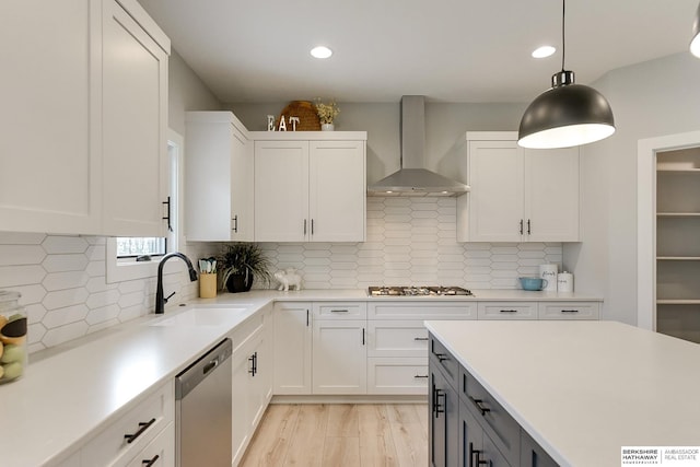 kitchen with stainless steel appliances, sink, wall chimney range hood, pendant lighting, and white cabinetry