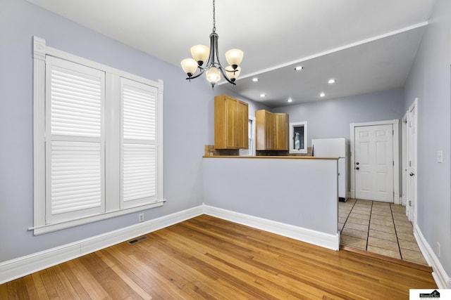 kitchen with white refrigerator, a notable chandelier, kitchen peninsula, pendant lighting, and light hardwood / wood-style floors