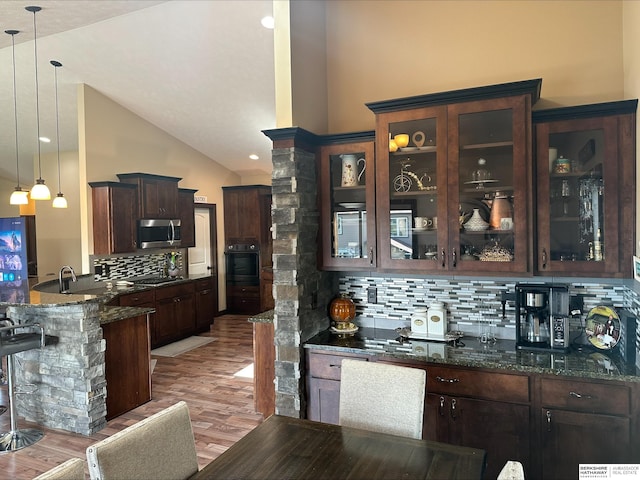 kitchen with backsplash, light hardwood / wood-style flooring, dark stone countertops, black oven, and hanging light fixtures