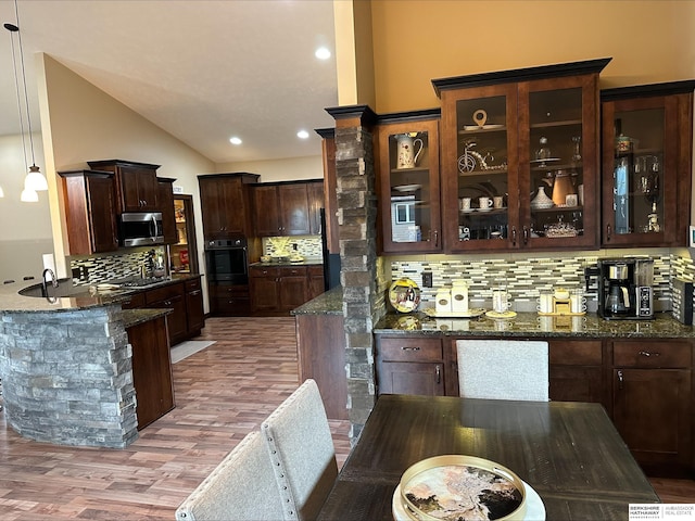 kitchen featuring backsplash, stainless steel appliances, wood-type flooring, pendant lighting, and dark stone countertops