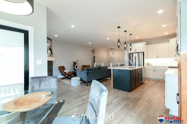 kitchen featuring pendant lighting, a center island with sink, white cabinets, light wood-type flooring, and stainless steel appliances