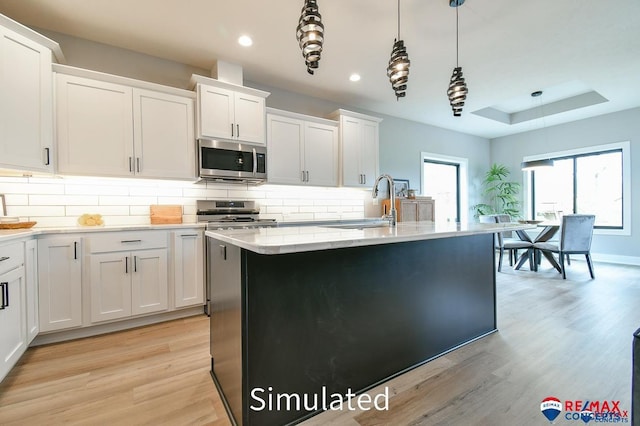 kitchen with light hardwood / wood-style flooring, decorative light fixtures, a center island with sink, white cabinets, and appliances with stainless steel finishes