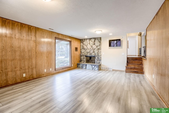 unfurnished living room featuring wood walls, a stone fireplace, and a textured ceiling