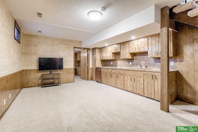 kitchen with a textured ceiling, light colored carpet, wooden walls, and sink