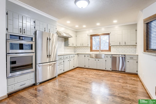 kitchen featuring wall chimney range hood, sink, decorative backsplash, white cabinetry, and stainless steel appliances