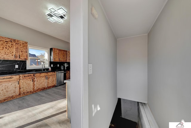 kitchen featuring sink, light hardwood / wood-style flooring, stainless steel dishwasher, ornamental molding, and tasteful backsplash