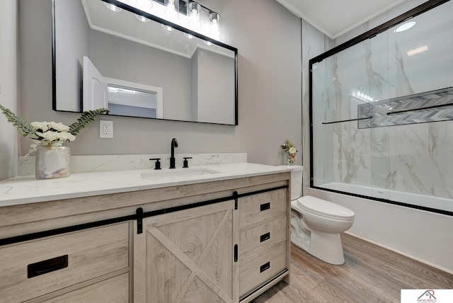 full bathroom featuring crown molding, hardwood / wood-style floors, toilet, shower / bath combination with glass door, and vanity