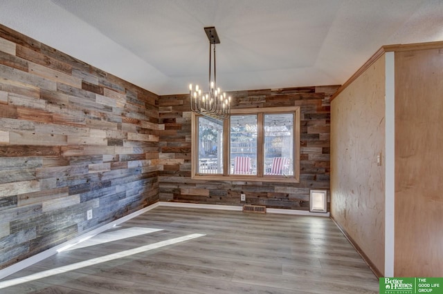 unfurnished dining area featuring wood walls, hardwood / wood-style floors, and a notable chandelier