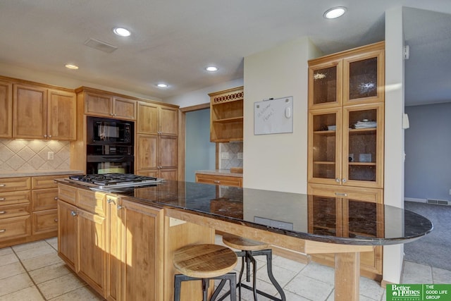 kitchen with tasteful backsplash, dark stone countertops, a breakfast bar, light tile patterned floors, and black appliances