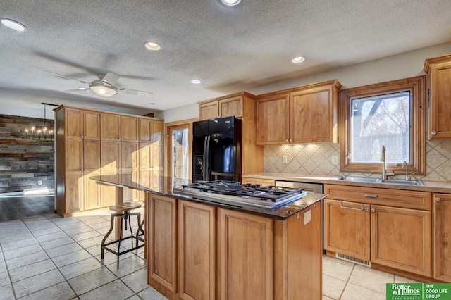 kitchen with stainless steel gas stovetop, black fridge, sink, decorative backsplash, and a kitchen island