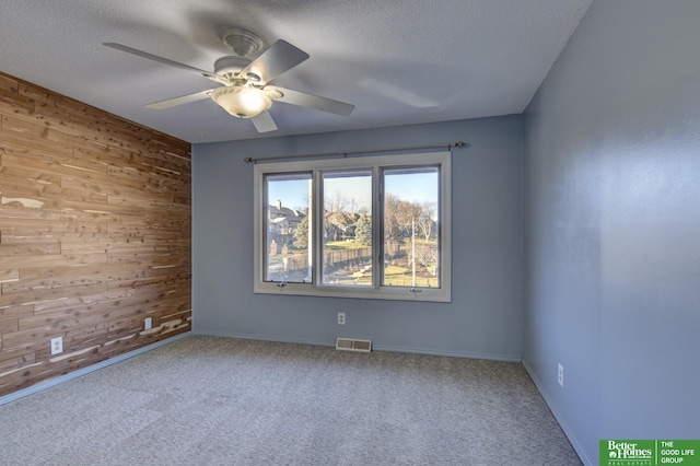 carpeted spare room with a textured ceiling, ceiling fan, and wood walls