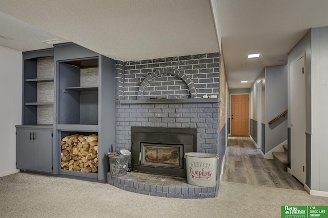 living room featuring hardwood / wood-style floors, built in shelves, a textured ceiling, and a brick fireplace