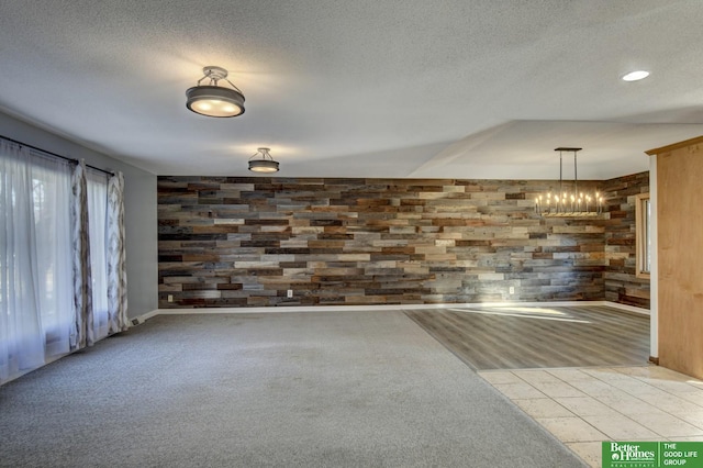 unfurnished room with carpet, wood walls, a textured ceiling, and an inviting chandelier