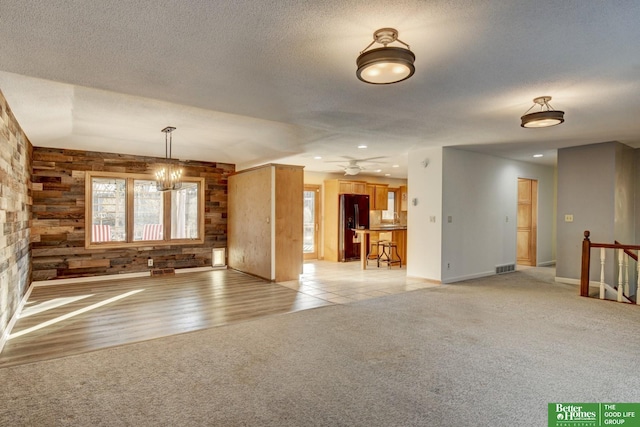 unfurnished living room with ceiling fan with notable chandelier, wood walls, light wood-type flooring, and a textured ceiling